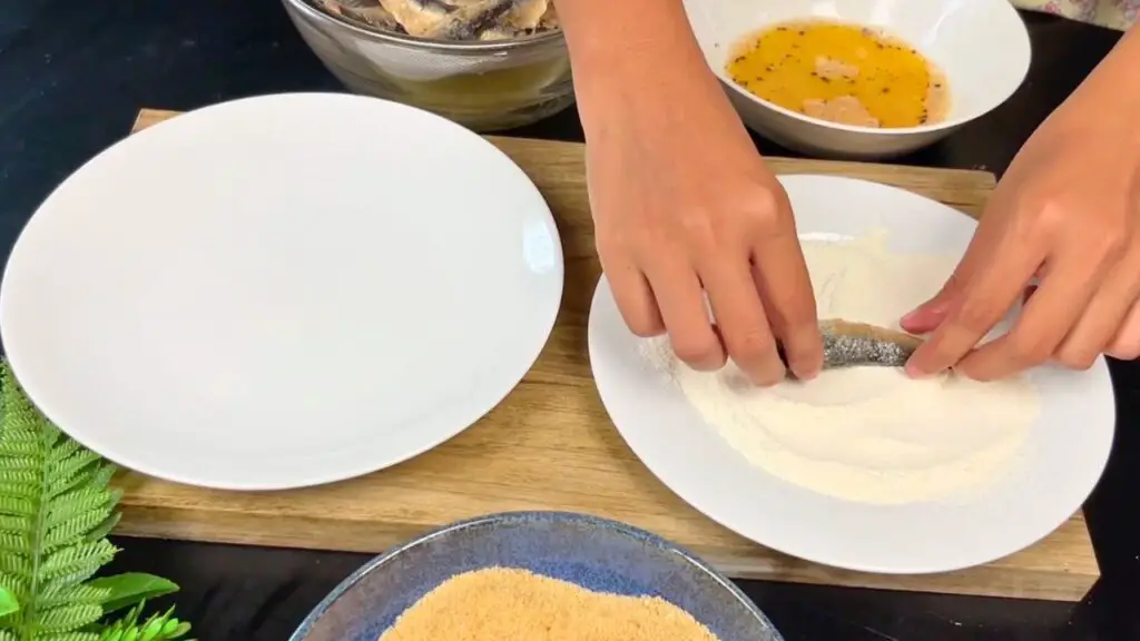 Crispy sardines step showing sardine being lightly coated in flour on both sides before cooking.