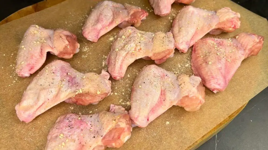 Raw chicken wings seasoned with spices on a tray, showing optional seasoning swaps like lemon pepper, Cajun, and barbecue rub.