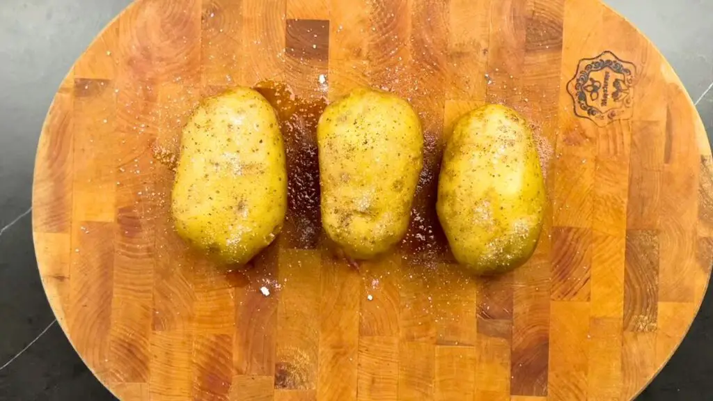 Air fryer baked potatoes cleaned and seasoned with oil, salt, and black pepper on a wooden cutting board before cooking.