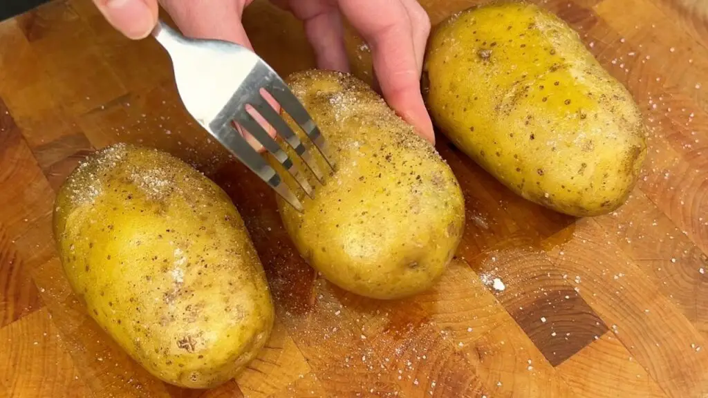 Air fryer baked potatoes recipe step showing potatoes being poked with a fork before cooking to release steam while air frying.