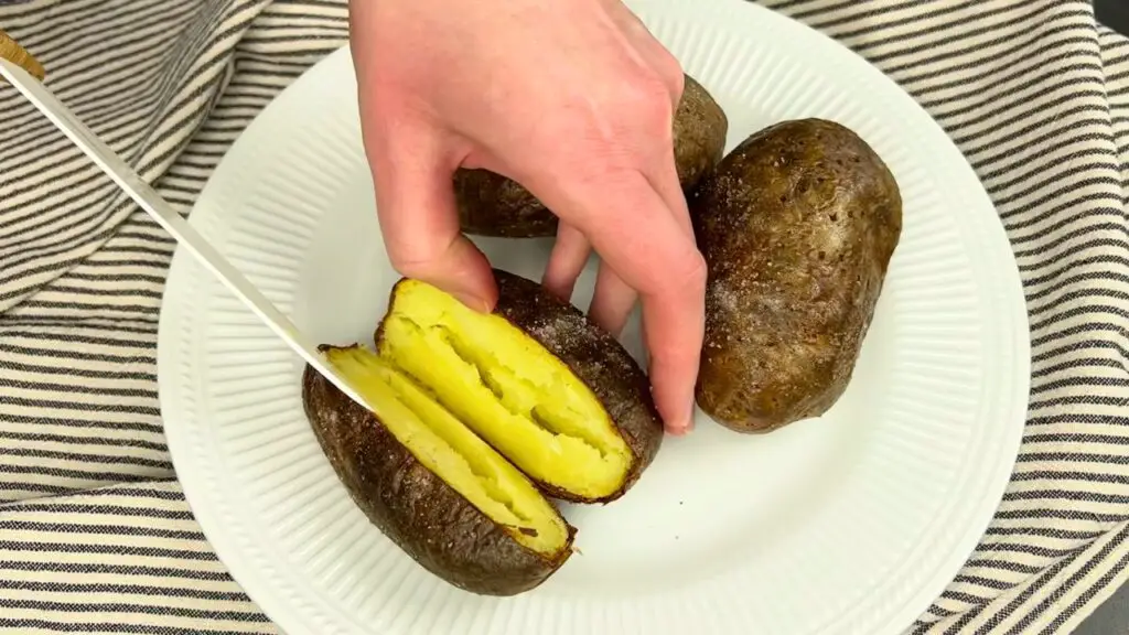 Air fryer recipes step showing baked potatoes being checked with a fork to see if the center is soft and fully cooked.