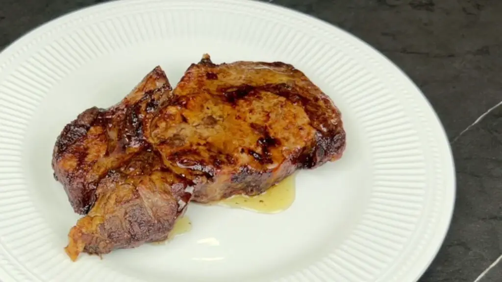 A golden-brown air fryer ribeye steak resting on a white plate with melted butter drizzled underneath, ready to rest before slicing in this easy air fryer ribeye steak recipe.