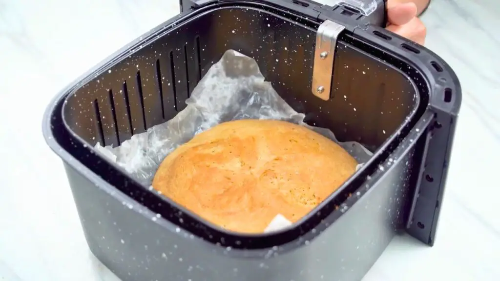 A hand brushing oil on a risen whole wheat bread dough in a parchment-lined air fryer basket.