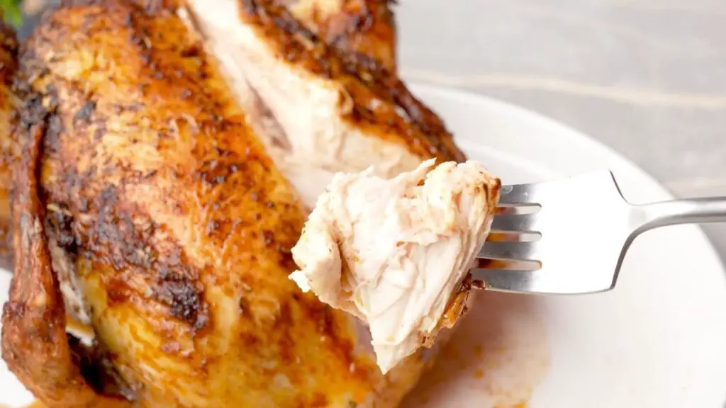 Close-up of a cooked whole chicken in an air fryer being sliced open, showing juicy white meat and crispy golden skin, a sign the chicken is fully cooked through.