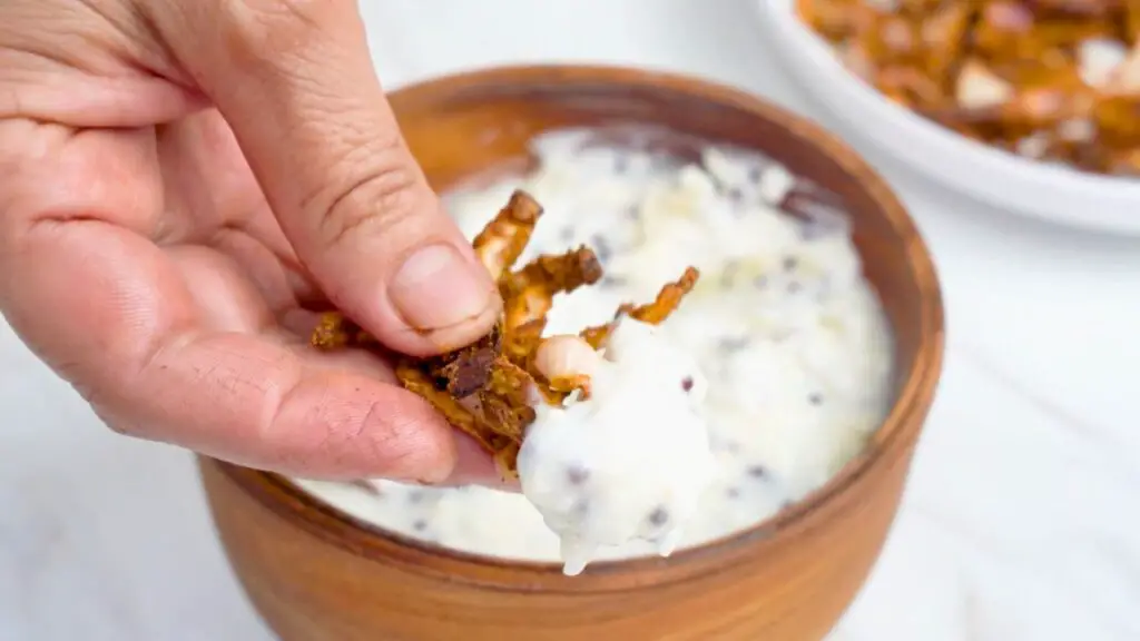 Crispy fried onions being dipped into a creamy cheesy garlic dip in a wooden bowl, showing a simple serving idea for this easy air fryer snack.