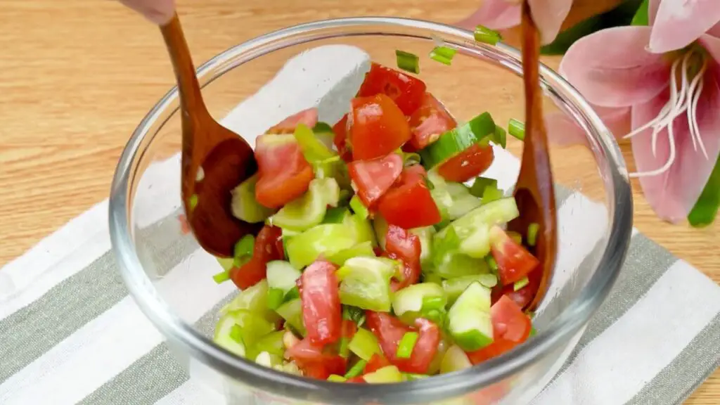 Easy chicken drumstick recipe served with a fresh salad of chopped tomatoes, cucumber, bell pepper, and spring onions being tossed in a glass bowl.