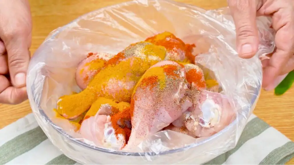 Easy chicken drumstick recipe with raw chicken drumsticks coated in paprika, turmeric, garlic, salt, and black pepper inside a plastic bag before mixing the seasoning.