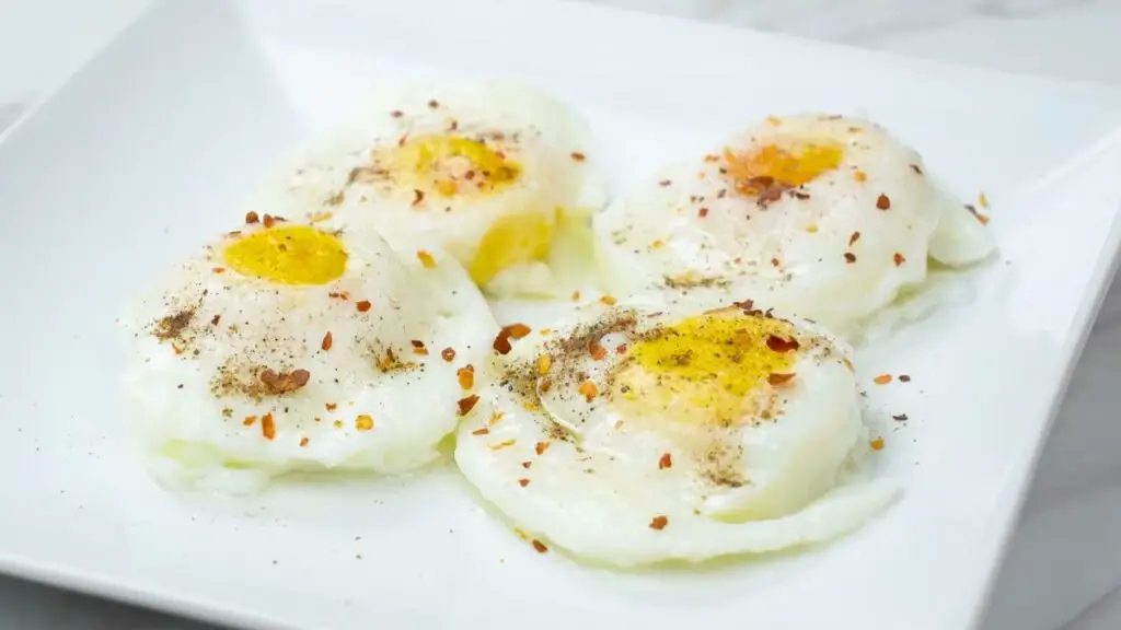 Four air fryer poached eggs served on a white plate, topped with black pepper and red pepper flakes, with tender whites and soft golden yolks ready to eat.