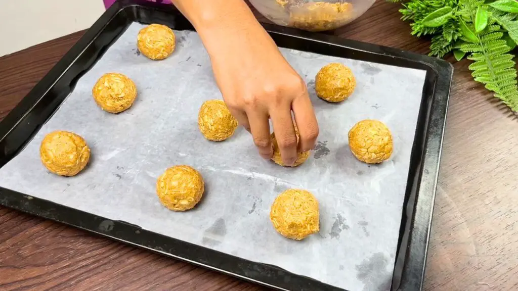 Hand placing peanut butter oatmeal cookie dough balls onto a parchment-lined baking tray, with evenly sized dough portions spaced apart and ready for baking.