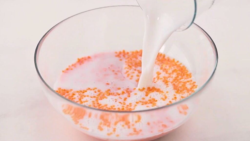 Milk being poured over red lentils in a clear glass bowl to soak overnight for red lentil waffles.
