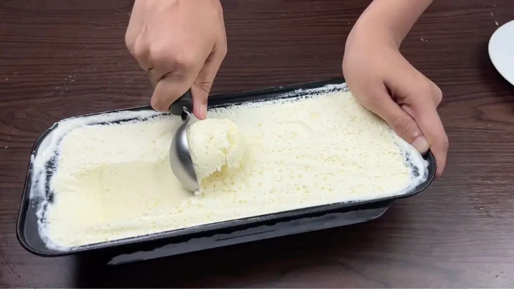 Scooping creamy homemade coconut ice cream from a loaf pan with an ice cream scoop, showing the smooth texture in this easy coconut ice cream recipe.