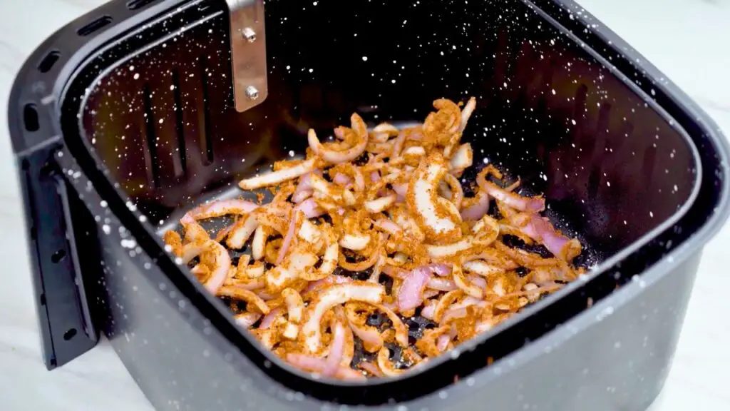 Seasoned onion slices spread in an air fryer basket, ready to cook into crispy fried onions.