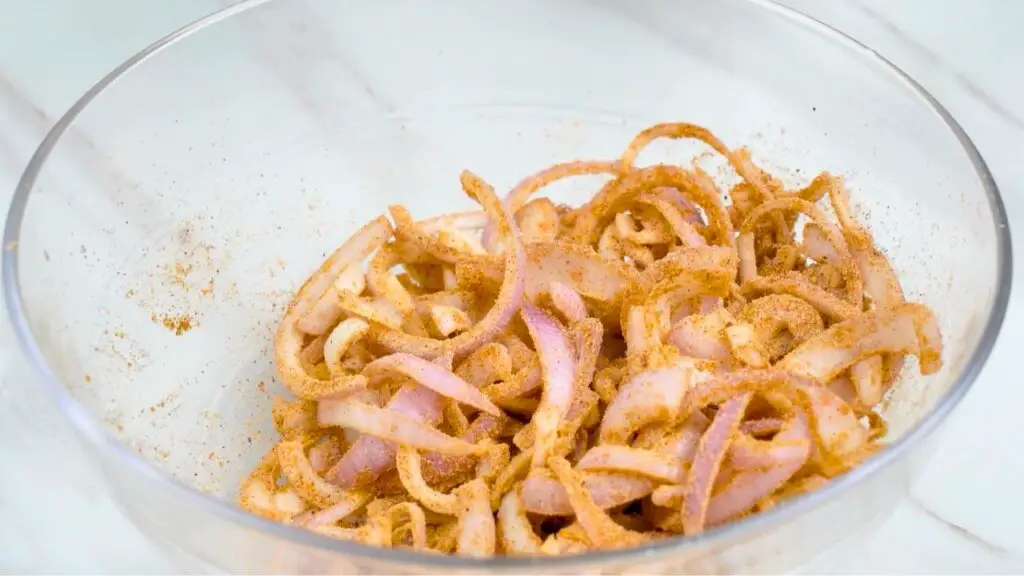 Sliced onions coated with seasoned flour mixture in a bowl, ready to cook as crispy air fryer onions.
