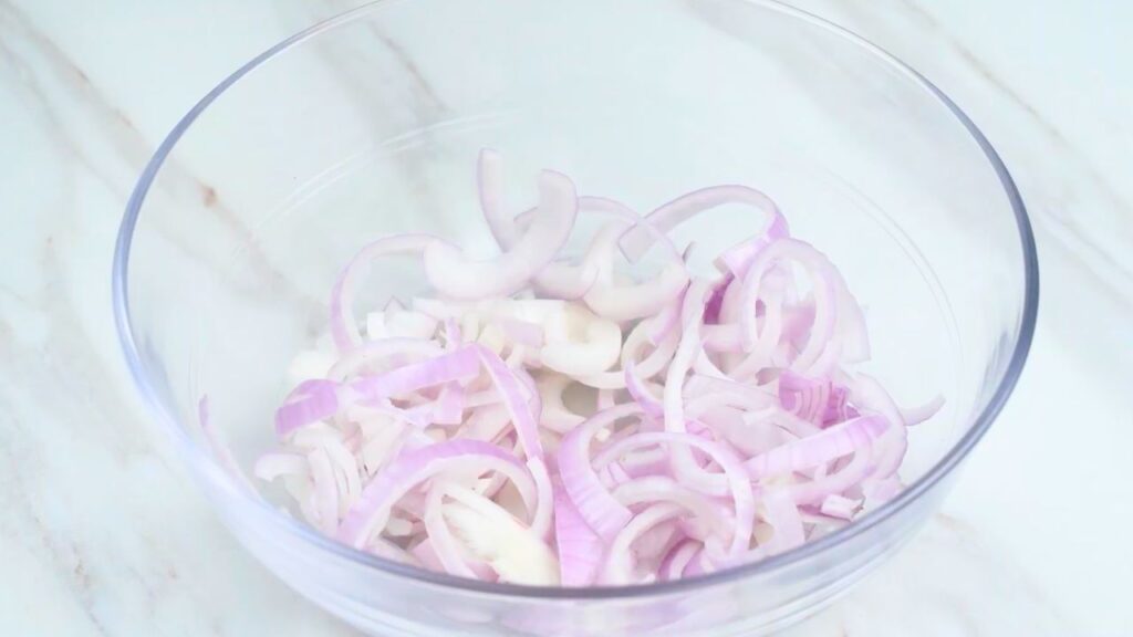 Sliced red onions in a mixing bowl, ready for seasoning and cooking