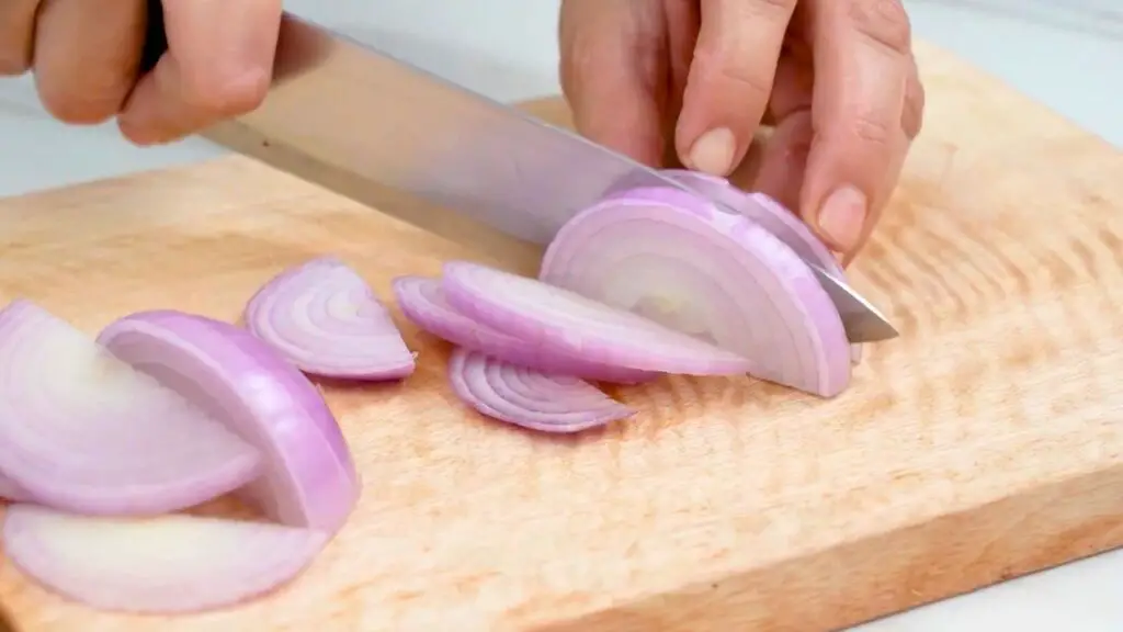 Slicing a red onion into thin, even half-moon slices on a wooden cutting board for fried onions in the air fryer.