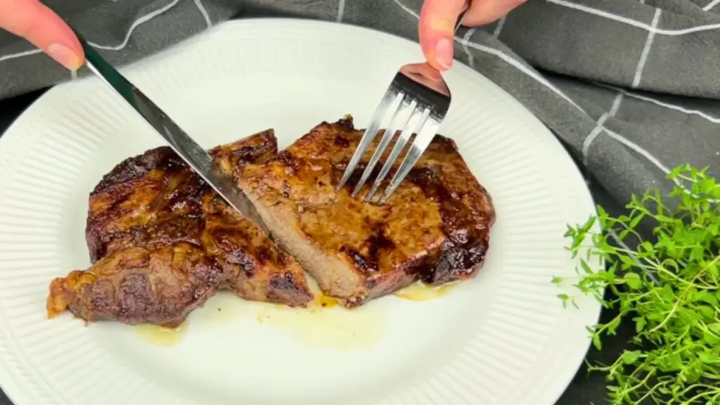 Slicing into a cooked ribeye on a white plate to reveal the inside during an easy air fryer steak recipe, showing the browned butter crust and juicy center after resting.