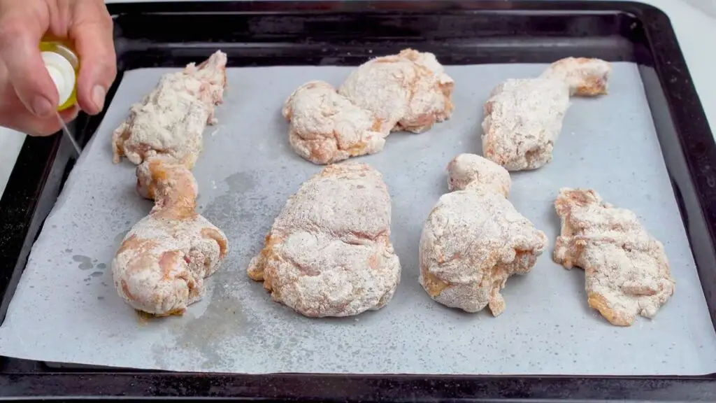 Spraying coated chicken with oil for crispy air fryer fried chicken.