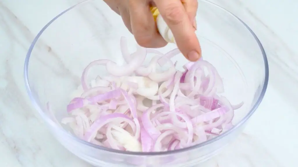 Spraying sliced red onions with oil in a mixing bowl before making crispy air fryer onions.