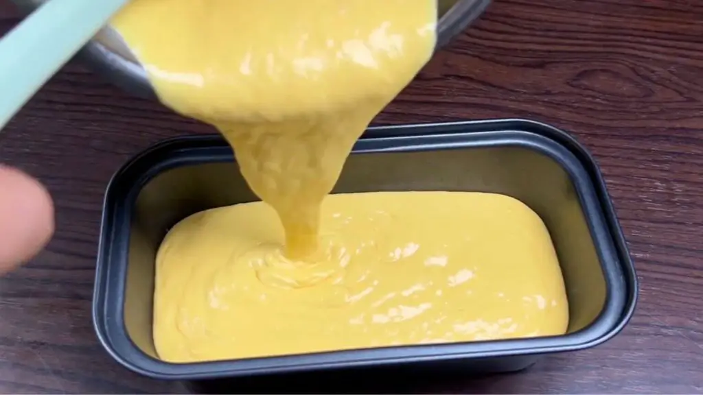 Thick and creamy mango ice cream mixture being poured from a bowl into a loaf pan, ready to be frozen into homemade mango ice cream.