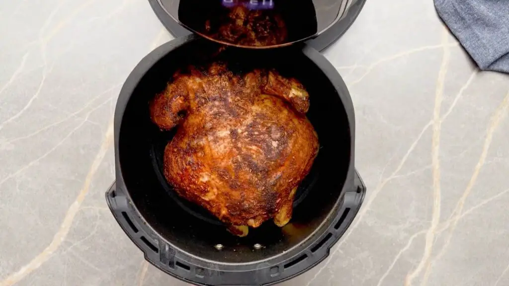 Whole chicken cooked in an air fryer basket with crispy browned skin, illustrating proper chicken size and spacing for even air fryer cooking.