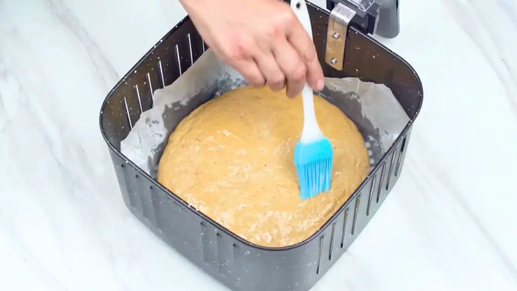 Whole wheat bread dough in an air fryer basket being brushed with oil before the final rise and baking.