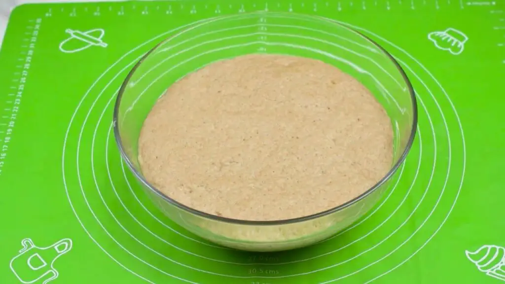 Whole wheat bread dough risen in a glass bowl on a green baking mat, looking puffy and doubled in size.