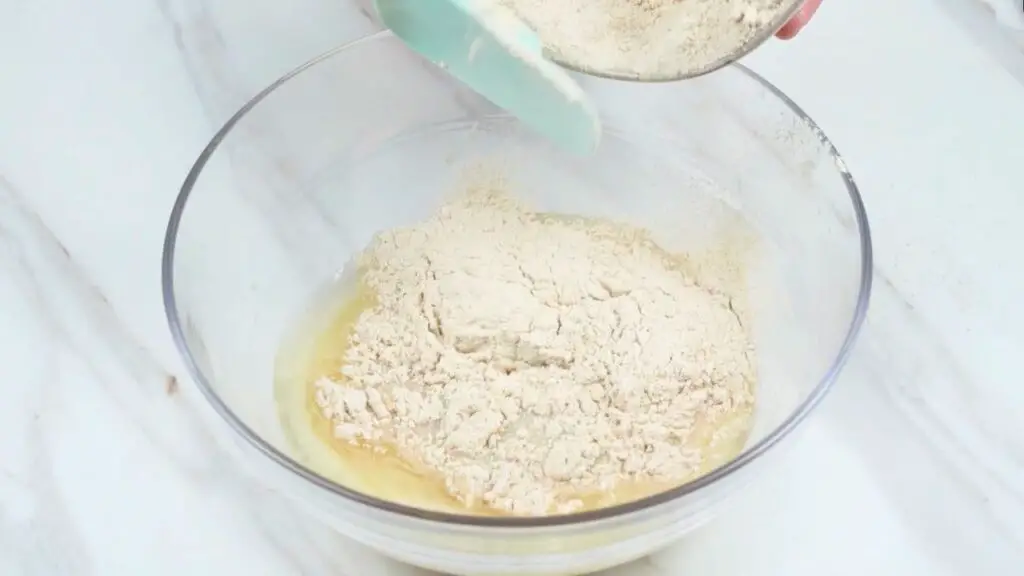 Whole wheat flour being added to a mixing bowl with wet ingredients while making healthy air fryer bread dough.
