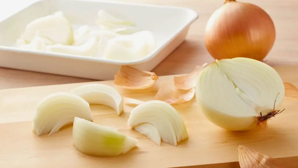Yellow and white onions on a wooden cutting board with sliced onion wedges, illustrating easy onion swaps
