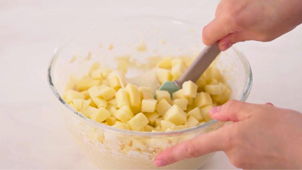 Apple waffle recipe showing diced fresh apples being gently folded into the waffle batter with a spatula so the apple pieces are evenly distributed before cooking.