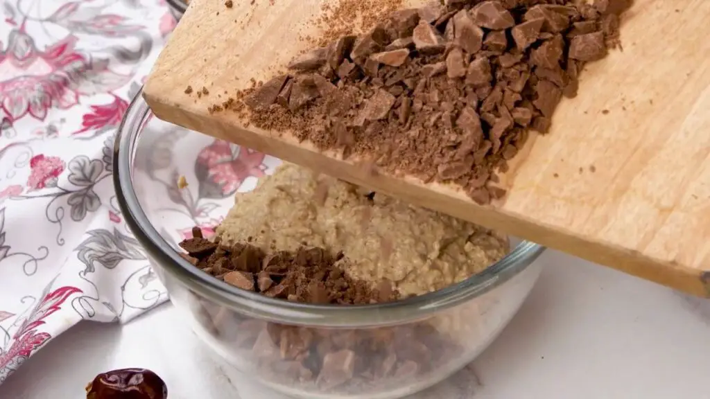 Chopped dark chocolate being folded into a creamy oat ice cream mixture before freezing.
