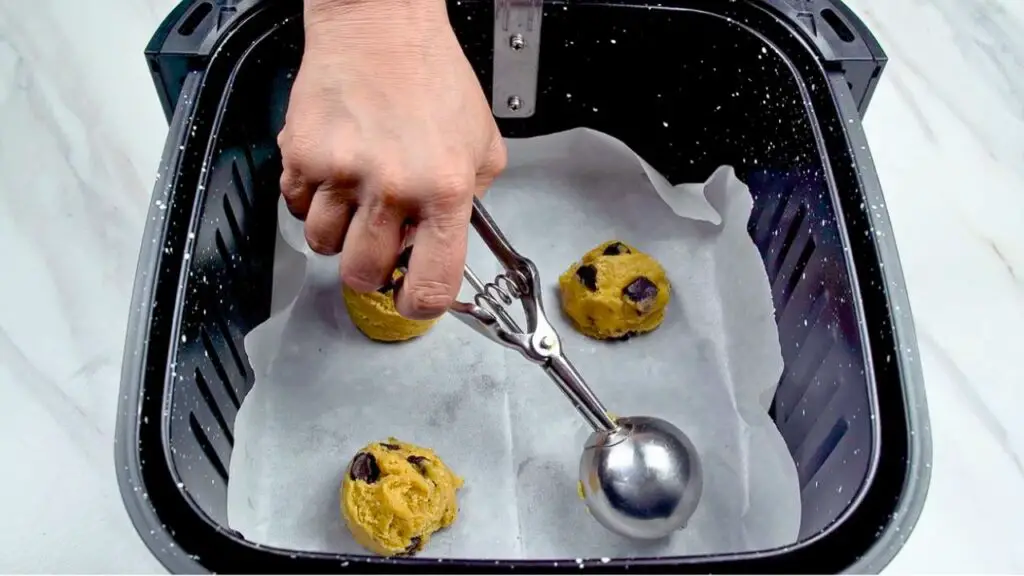 Cookie dough scooped into an air fryer basket lined with parchment paper, ready to bake into cookies in the air fryer.