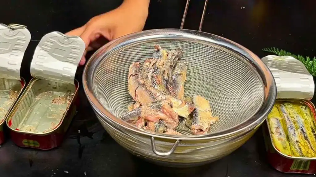 Crispy fried sardines recipe showing canned sardines draining in a fine-mesh sieve after being removed from their tins, ready to be coated before frying.
