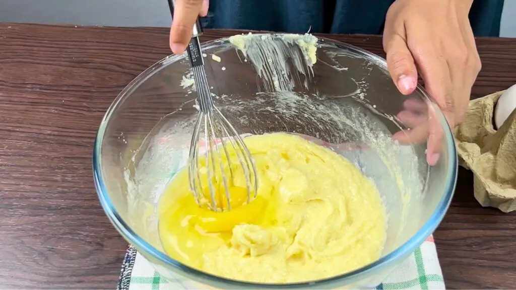 Egg being whisked into the butter and sugar mixture while making Starbucks-style lemon pound cake batter in a glass mixing bowl.