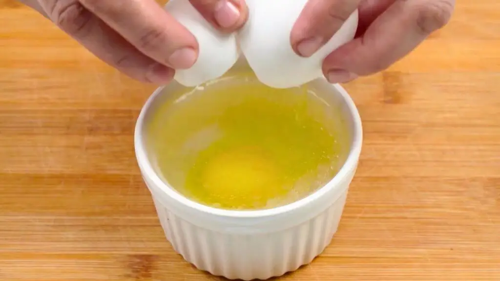 Fresh egg being cracked into a ramekin of hot water for an air fryer poached egg on toast.