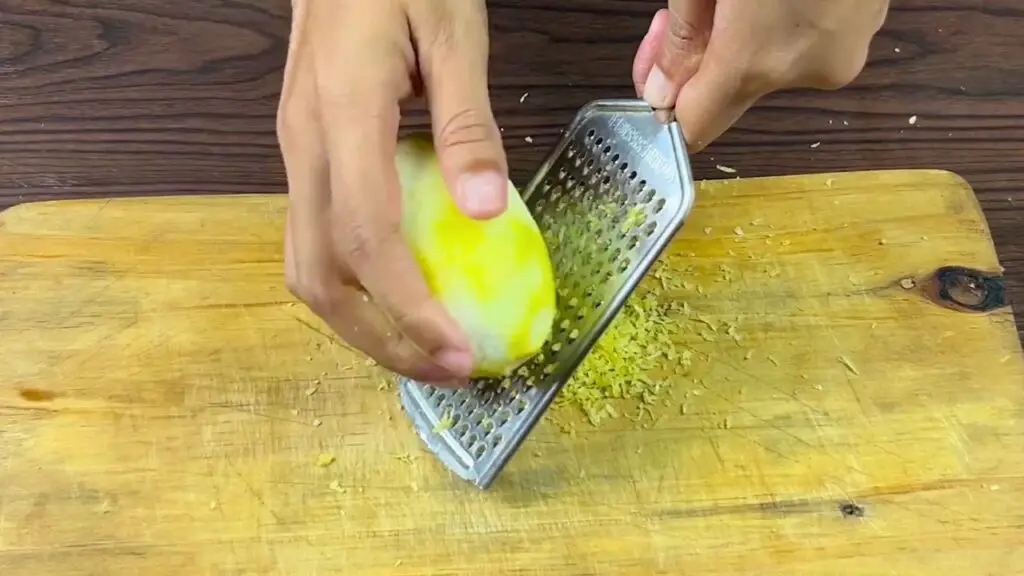 Fresh lemon being finely zested with a handheld grater for a Starbucks-style lemon loaf recipe.