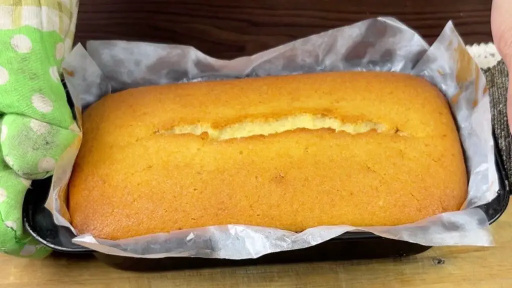 Freshly baked Starbucks-style lemon pound cake cooling in a parchment-lined loaf pan with a golden top and a natural crack down the center.