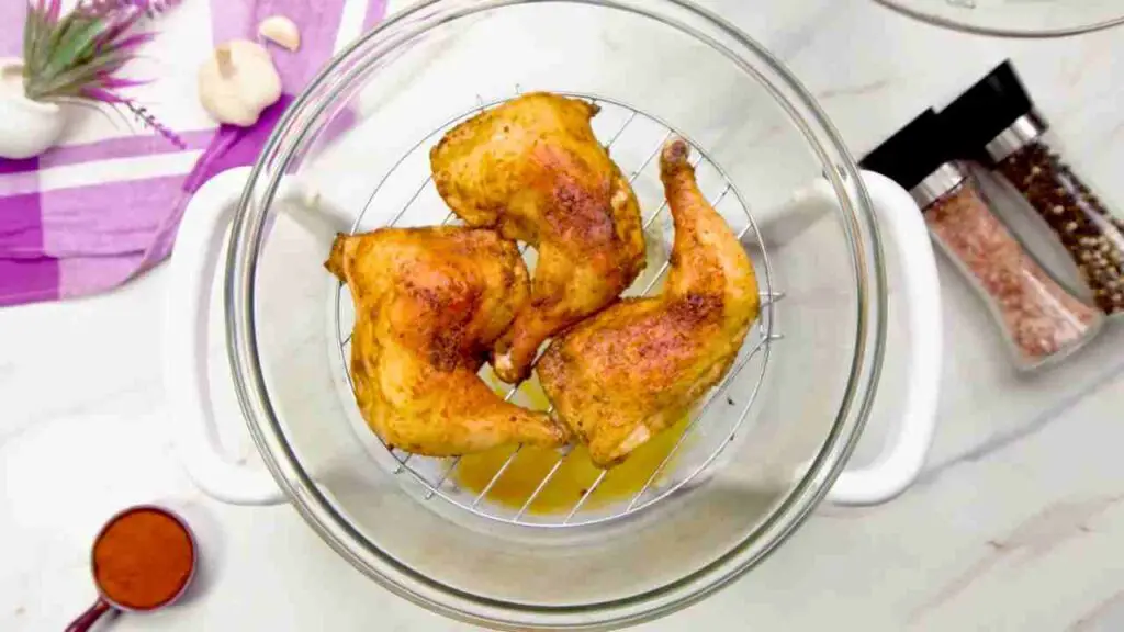 Golden, crispy chicken legs in the air fryer cooking inside a glass halogen air fryer bowl.