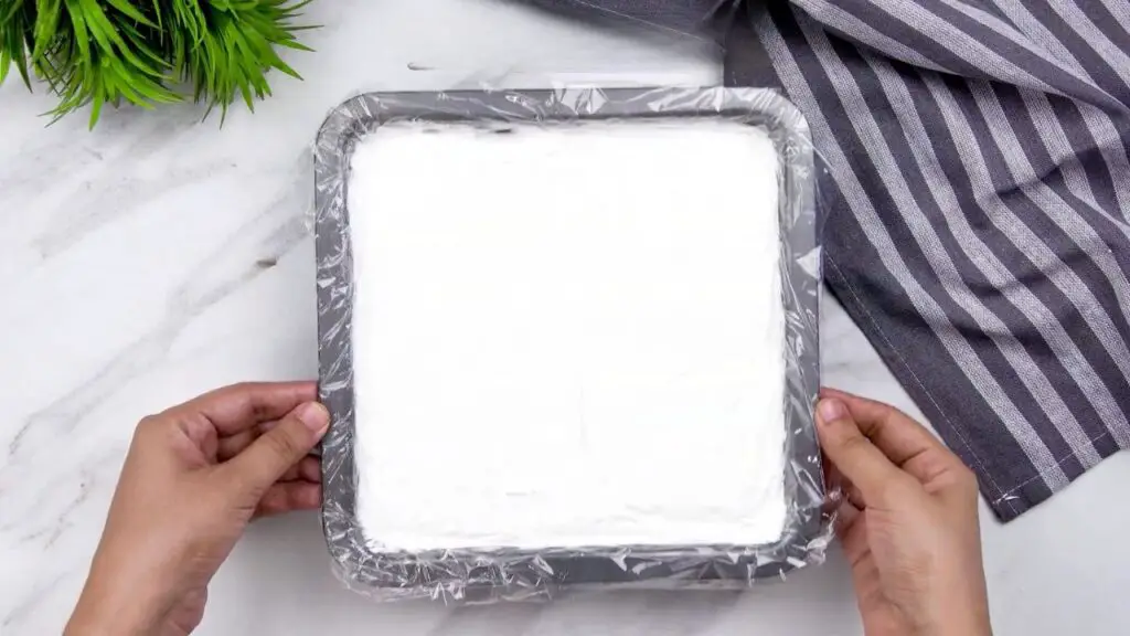 Homemade ice cream recipe covered with plastic wrap in a freezer-safe pan, ready to freeze overnight.