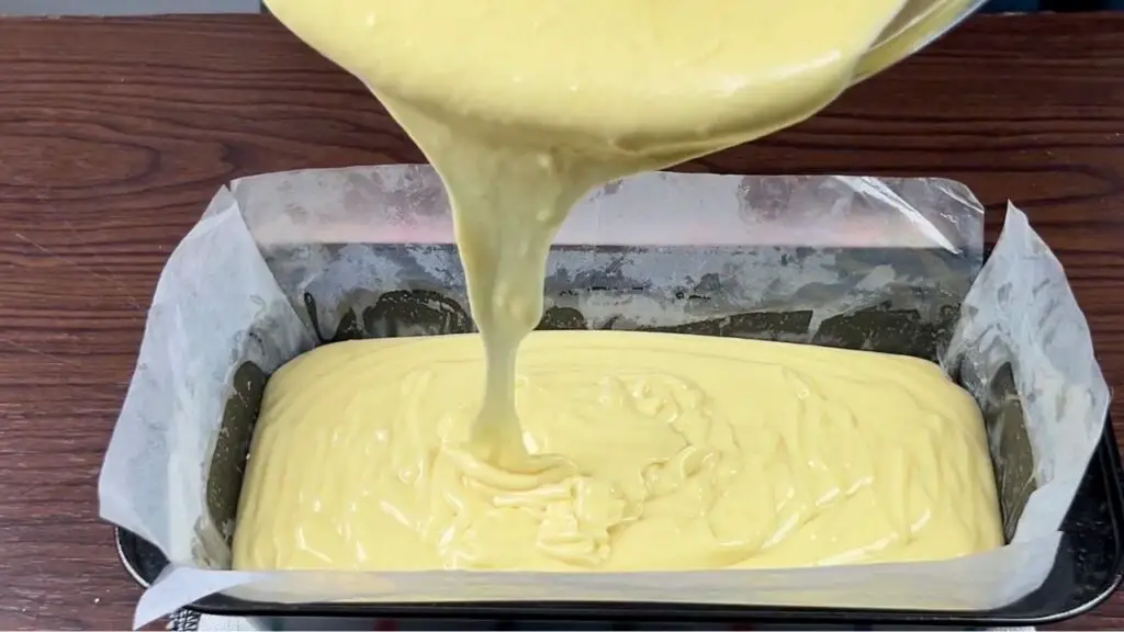 Lemon loaf batter being poured into a parchment-lined loaf pan before baking a homemade Starbucks lemon loaf.