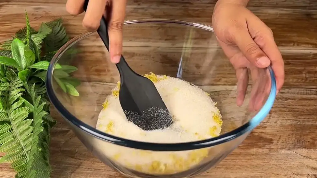 Mixing granulated sugar with fresh lemon zest in a bowl to make a fragrant lemon poppy seed cake batter.