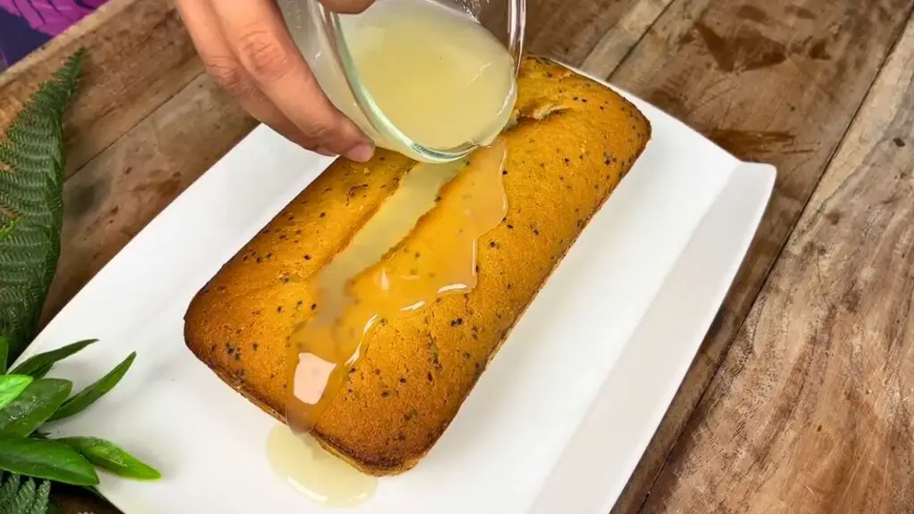 Moist lemon loaf recipe topped with a fresh lemon glaze being poured over the golden poppy seed loaf cake.