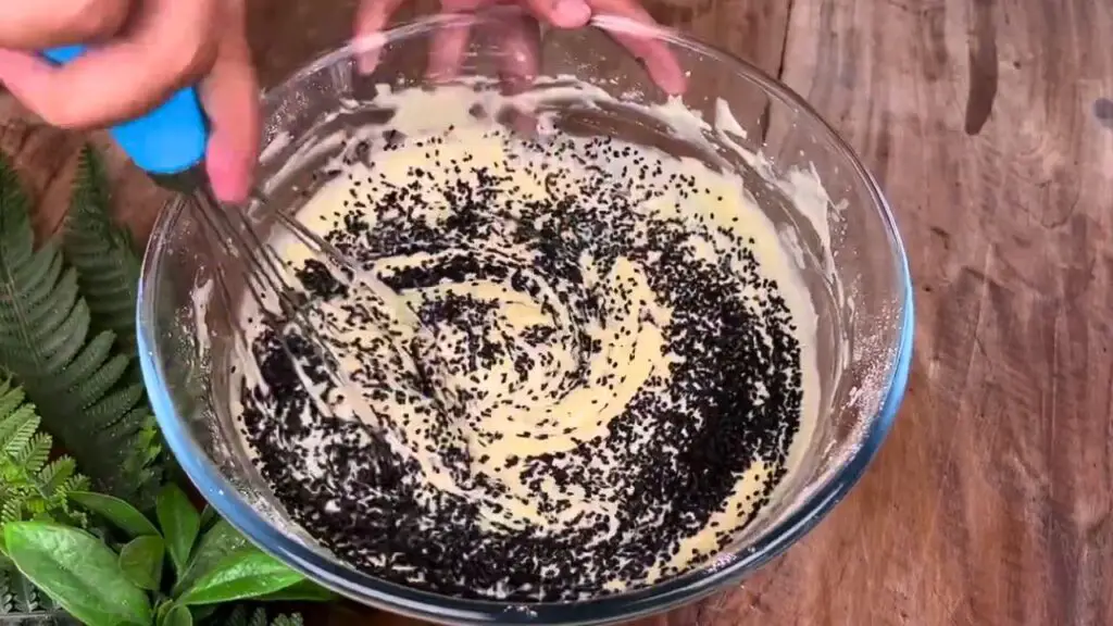 Moist lemon poppy seed loaf cake batter being whisked with poppy seeds evenly mixed throughout in a glass bowl.