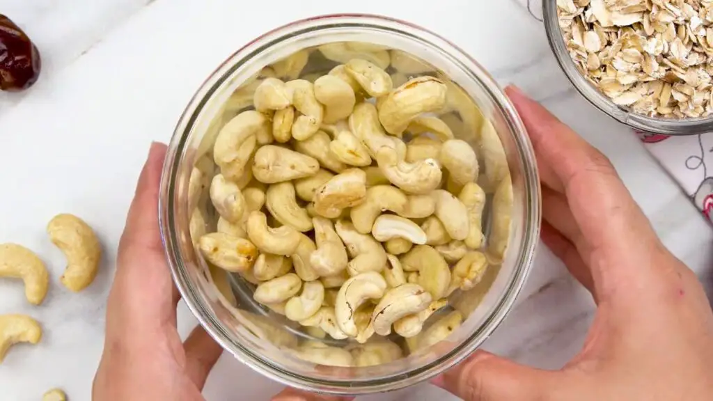 Oat ice cream recipe showing raw cashews soaking in warm water in a blender cup to soften before blending into a smooth and creamy dairy-free ice cream base.