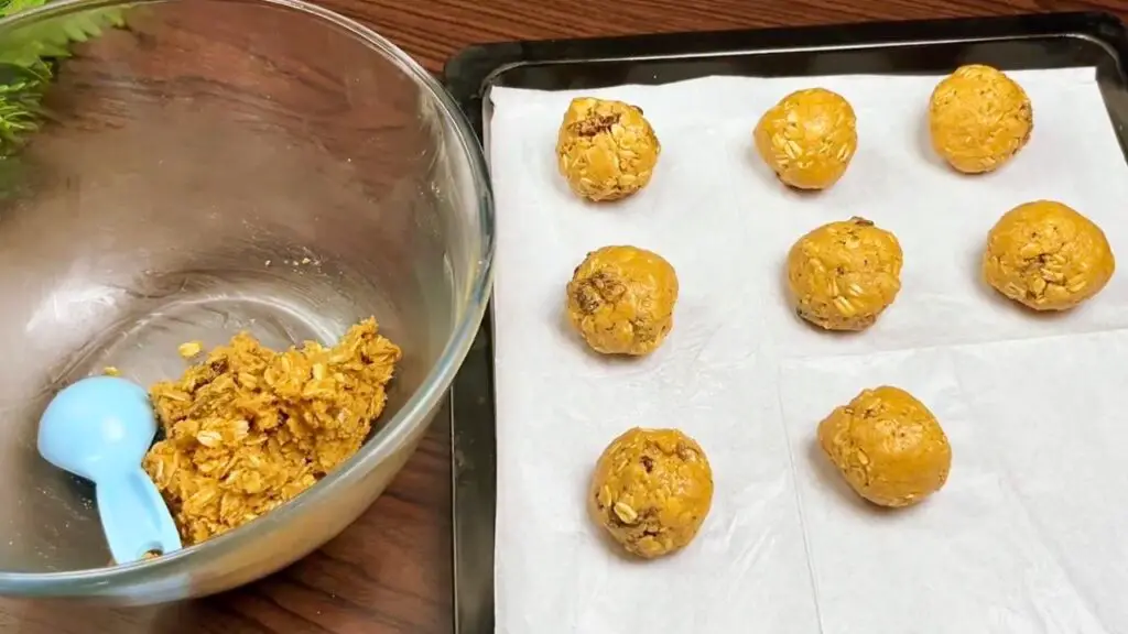Oatmeal peanut butter cookies with dough balls shaped and arranged on a parchment-lined baking tray before baking.