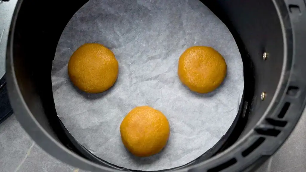 Peanut butter cookie dough balls spaced apart in an air fryer basket, ready for baking.