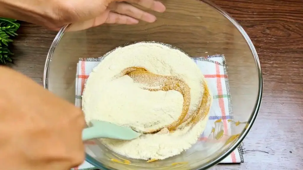 Peanut butter oatmeal cookies recipe showing brown sugar being mixed into creamy peanut butter in a glass bowl.