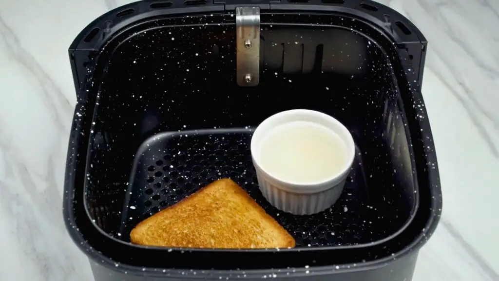 Poached eggs in air fryer cooking in a ramekin beside toast inside the air fryer basket.
