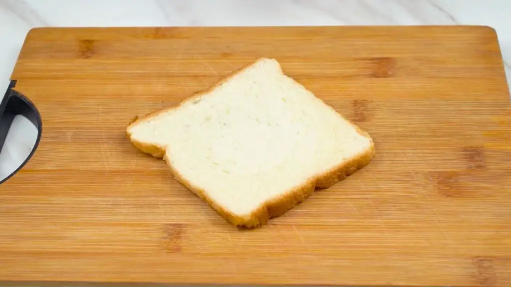 Slice of soft white sandwich bread on a wooden cutting board for making air fryer poached eggs.