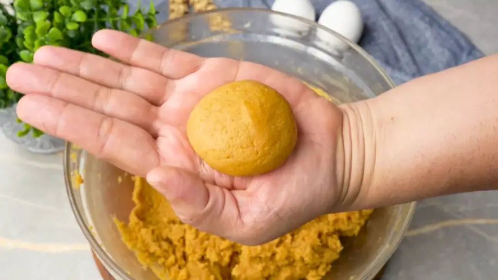 Smooth ball of peanut butter cookie dough held in a hand before placing it in the air fryer basket.