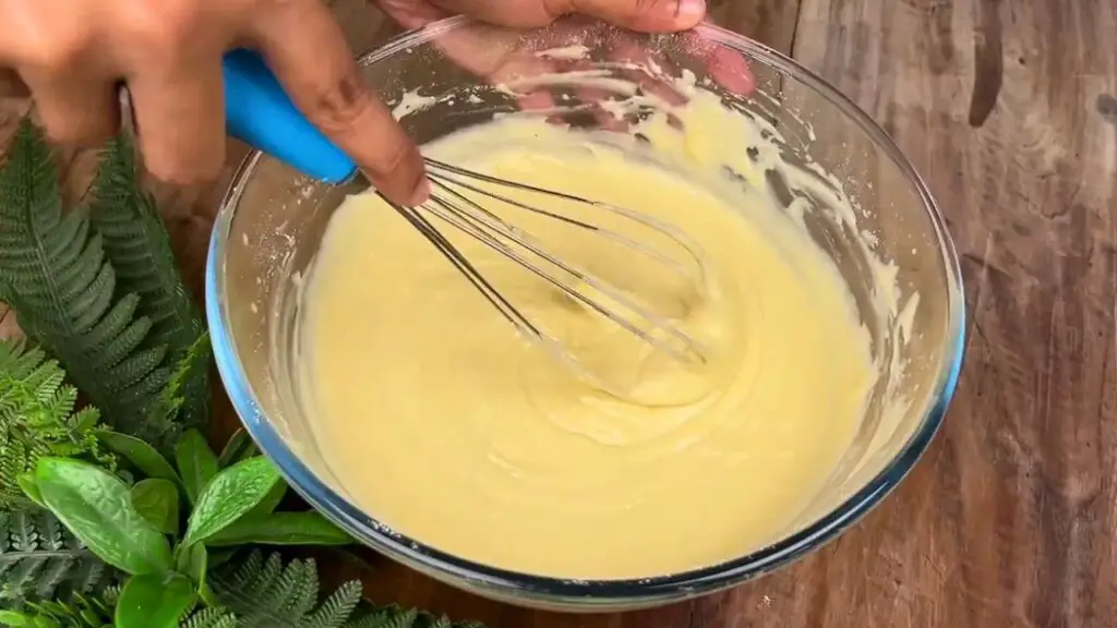 Smooth lemon poppy seed loaf cake batter being whisked in a glass mixing bowl until creamy and lump-free.